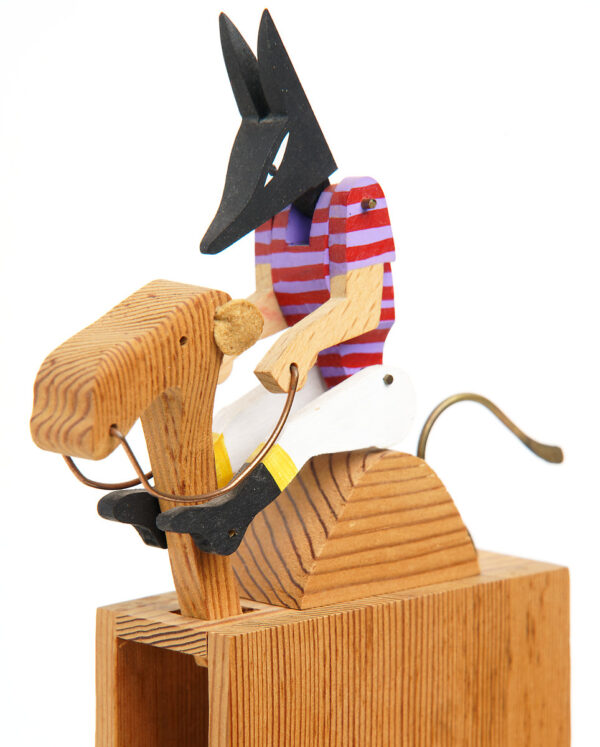 The Anubis is wearing a striped shirt and riding a camel. Carved wooden automata.