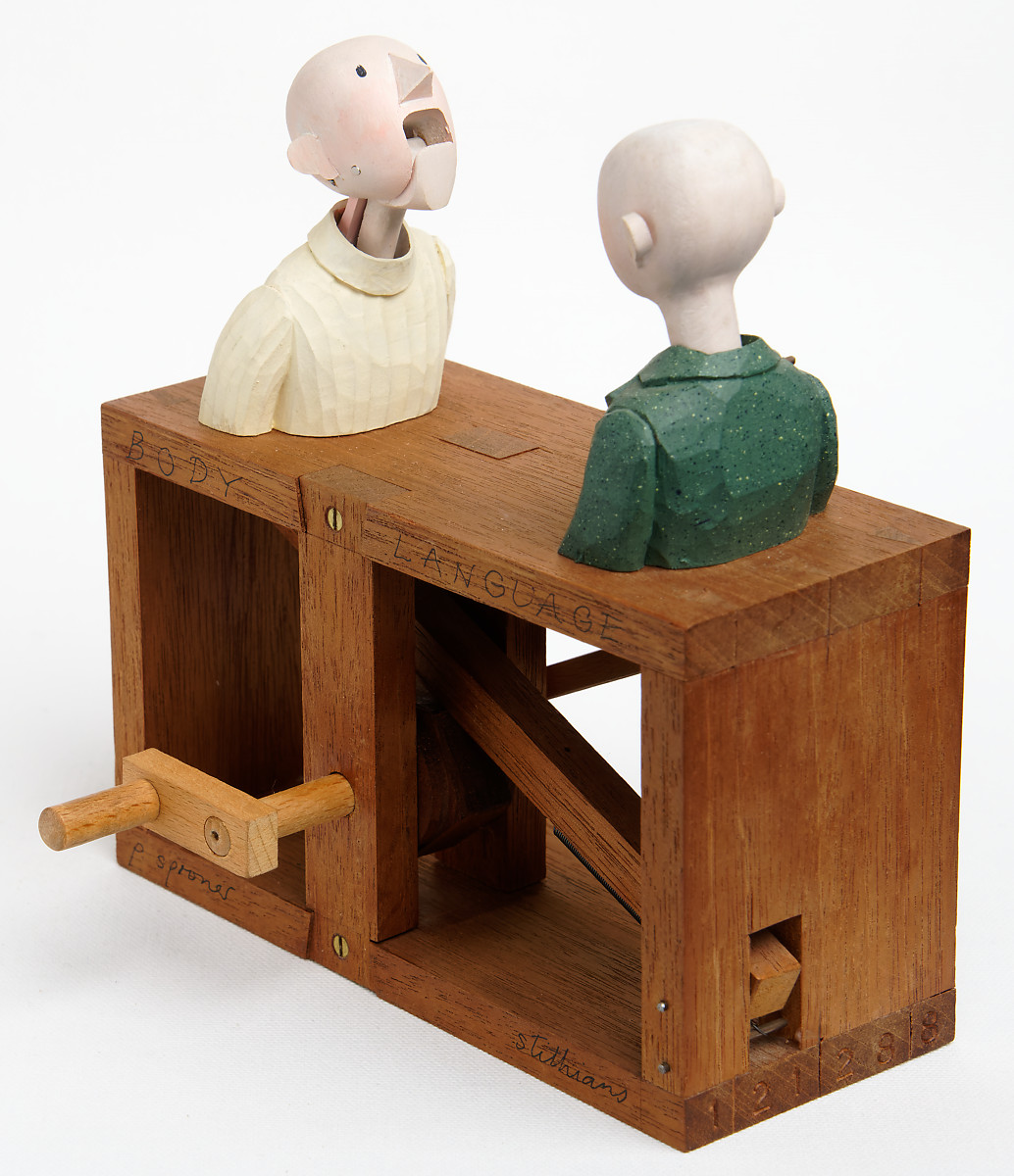 Carved painted wooden automata. 2 bald men are in conversation. One speaks and the other nods.