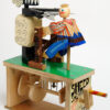Brightly painted carved wooden automata. A sheep stands upright shearing a mans hair.