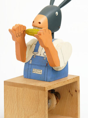 Carved painted wooden automata. A Donkey in blue dungarees and white shirt, eats a corn on the cob.