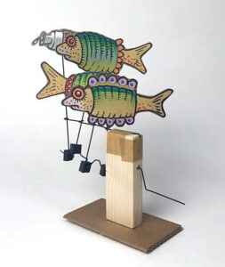 Two painted cardboard fish wearing frilly jumpers attached to a simple crank mechanism.