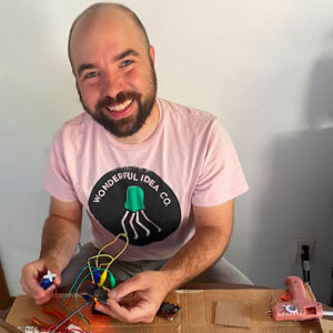 Ryan is smiling at the camera and holding wires and components