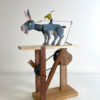Hand carved and painted donkey with a yellow bird on his back.He stands on a wooden platform on an open frame contains cams, pulleys and levers.