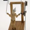 A carve wooden figure with a sad expression jumps with a skipping rope.