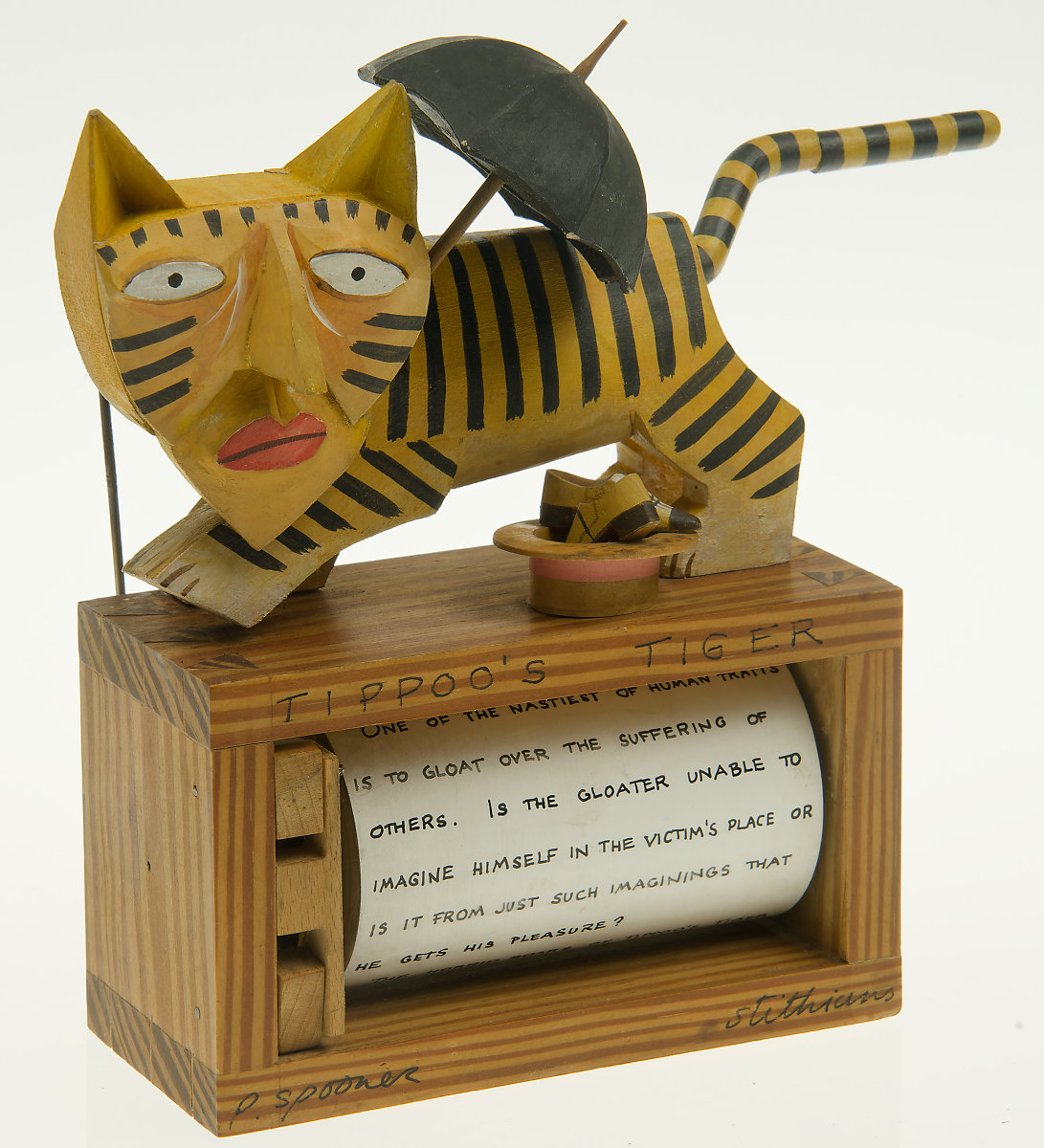 A carved wooden tiger holding an umbrella. A hat and shoes are in front of him. There is a barrel with text in the box below him.