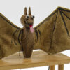 A carved wooden bat with fabric wings sticks out a bright red tongue.