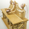 3 carved figures with painted faces sit at a table demonstrating the properties of solid, liquid and gas.